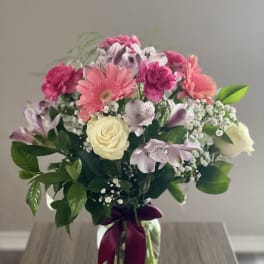 Mixed pink and white bouquet in a glass vase with a purple ribbon