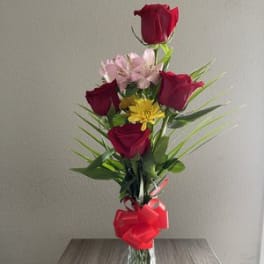 Tall bouquet of red roses and pink flowers in a glass vase with a red bow