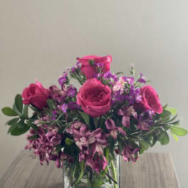 Pink roses and purple flowers arranged in a clear glass vase.