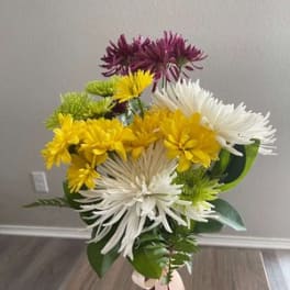 Bouquet of white, yellow, green, and purple chrysanthemum blooms in a pink vase