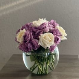 Purple and white roses in a round glass vase