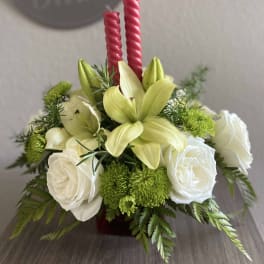 White roses and pale yellow lilies arranged with red candles.