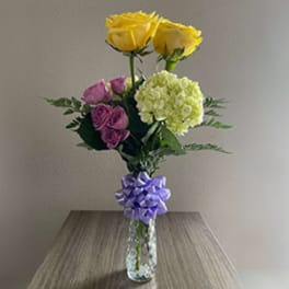 Bouquet of yellow and pink roses with a green hydrangea in a glass vase