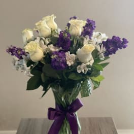 Bouquet of cream roses and purple flowers in a glass vase with a purple ribbon