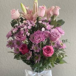 Pink roses and lilies arranged in a glass vase with a white ribbon