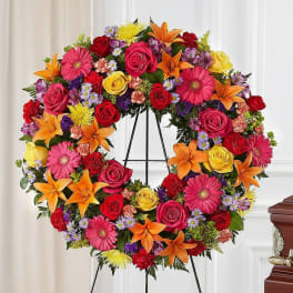 Colorful floral wreath on a black stand with roses, lilies, and daisies