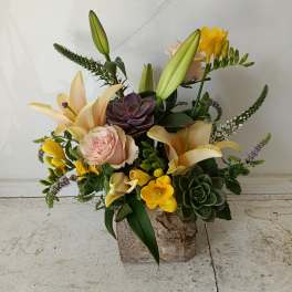 Mixed floral arrangement with lilies, roses, and succulents in a rustic container