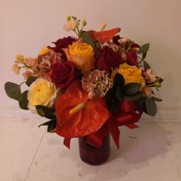 Bouquet of red and yellow roses with orange anthuriums in a dark vase
