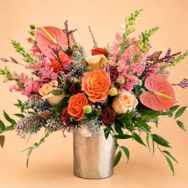 Mixed bouquet of orange and pink flowers in a silver vase