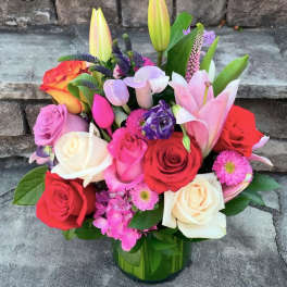 Colorful arrangement of roses, lilies, tulips, and mixed blooms in a clear glass vase