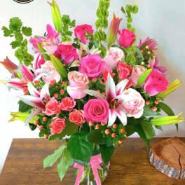 Tall mixed bouquet of pink roses and white-pink lilies in a clear glass vase with a pink ribbon.