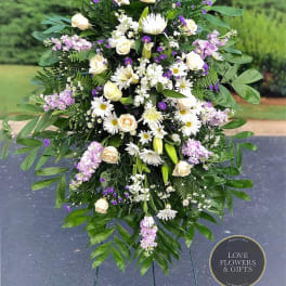 Tall standing spray of white and cream flowers with purple accents on an easel stand