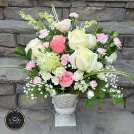Tall arrangement of white and pink roses with pink carnations and green hydrangea in a white urn vase.