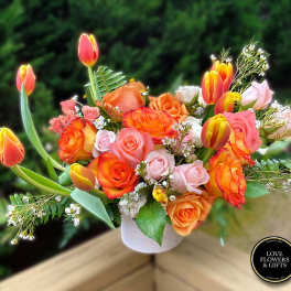 Arrangement of orange and pink roses with yellow-orange tulips in a white vase