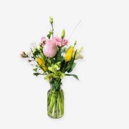 Tall mixed bouquet of pink and yellow flowers in a clear glass vase.