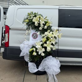 White lily floral wreath with large white bows on a stand