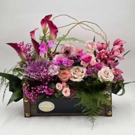 Pink and purple floral arrangement in a wooden box with roses and calla lilies