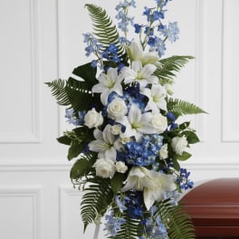 White lilies and blue flowers arranged on a funeral easel beside a casket