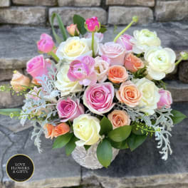 Pastel roses and ranunculus arranged in a white ceramic vase.