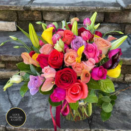 Colorful bouquet of roses, calla lilies, and lilies in a clear glass vase on stone steps