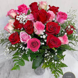 Arrangement of red and pink roses with white filler flowers in a textured glass vase