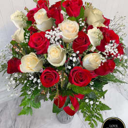Tall vase arrangement of red and cream roses with baby's breath and a red ribbon