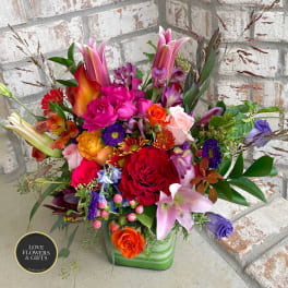 Colorful mixed bouquet with lilies, roses, and assorted blooms in a green glass cube vase