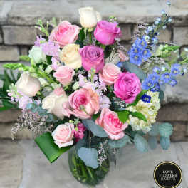 Mixed bouquet of pink and white roses with blue delphinium in a clear glass vase.