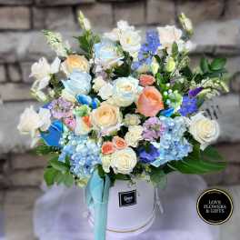 Pastel roses, hydrangeas, and mixed blooms arranged in a white hat box with aqua ribbon.