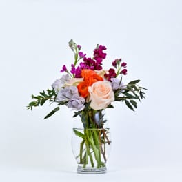 Bouquet of peach, orange, and lavender flowers in a clear glass vase