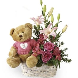 Teddy bear in a basket with pink flowers and lilies