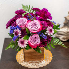 Pink roses and purple flowers arranged in a wooden box