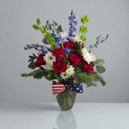 Red roses and white daisies in a glass vase with a patriotic ribbon