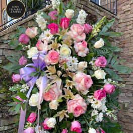 Tall standing spray of pink and white roses, lilies, and daisies with a lavender ribbon on an easel