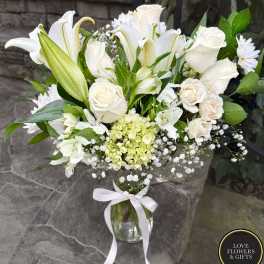 Tall white flower arrangement in a clear glass vase with a white ribbon bow