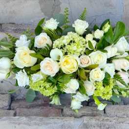 Low arrangement of white and cream roses with soft green blooms in an elongated design