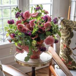 Pink and purple floral arrangement in a decorative vase on a small table