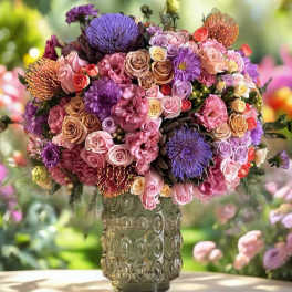 Large mixed bouquet in a patterned glass vase with pink, purple, and peach flowers