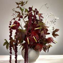 Deep red floral arrangement in a round vase with trailing burgundy blooms