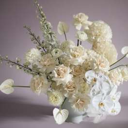 Cream and white floral arrangement in a white vase with orchids and roses