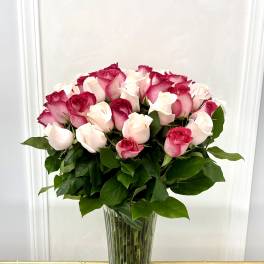 Pink and white roses arranged in a tall clear glass vase