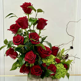 Red roses arranged in a low gray vase with green hydrangeas