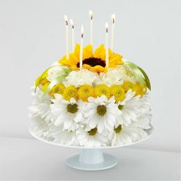 Flower cake with white daisies, yellow blooms, and lit candles