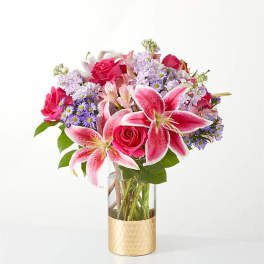 Pink lilies and roses in a clear vase with a gold base