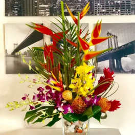 Tropical flower arrangement in a clear square vase with red, yellow, and purple blooms