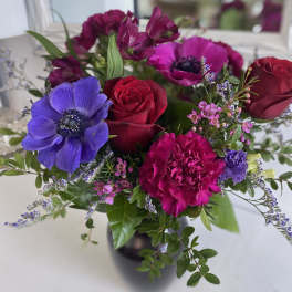 Vase arrangement of red roses, magenta carnations, and purple anemones with small pink blooms