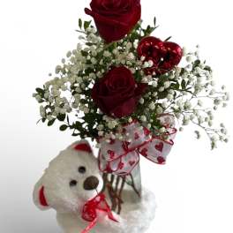 Small vase with red roses, baby's breath, heart pick, and a white teddy bear.