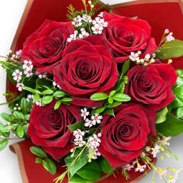 Hand-tied bouquet of red roses with tiny pink filler flowers wrapped in red paper.