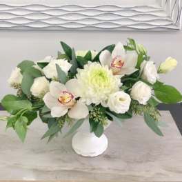 White floral arrangement in a white vase with orchids and chrysanthemums