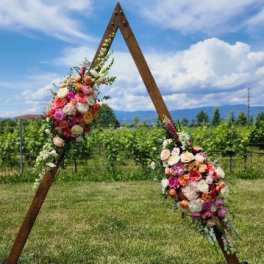 Triangle wooden arch decorated with pink, peach, and white flower clusters in an outdoor field